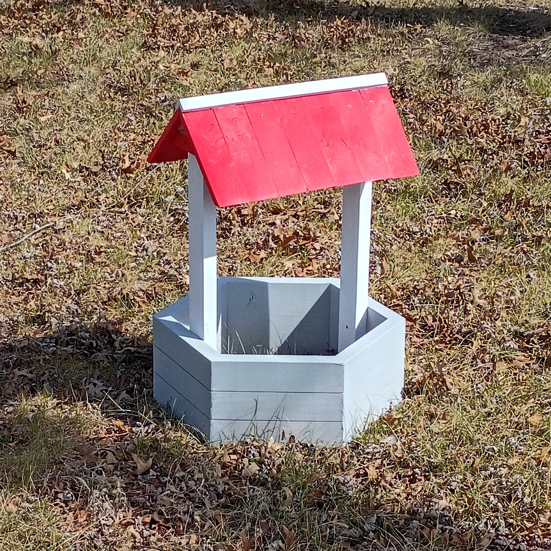 Small concrete well with red cover on grass in front of a brick building
