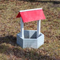 Small concrete well with red cover on grass in front of a brick building